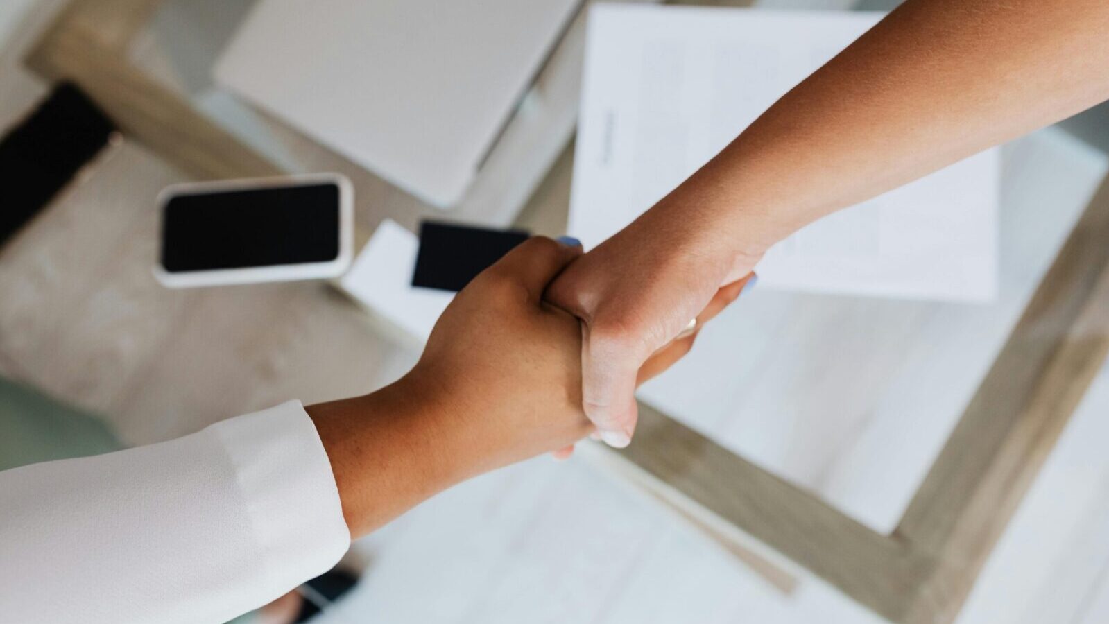 Two people shaking hands over a desk with modern tech, symbolizing a successful business agreement.